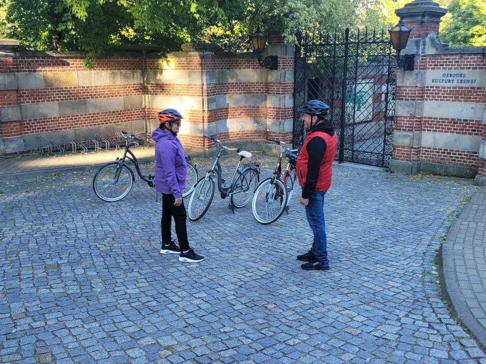 Dwoje rowerzystów w kaskach stojących z rowerami przed zabytkową ceglana bramą wejściową do Ośrodka Kultury Leśnej w Gołuchowie. Zapraszamy do Agroturystyki "Pod Bocianem"